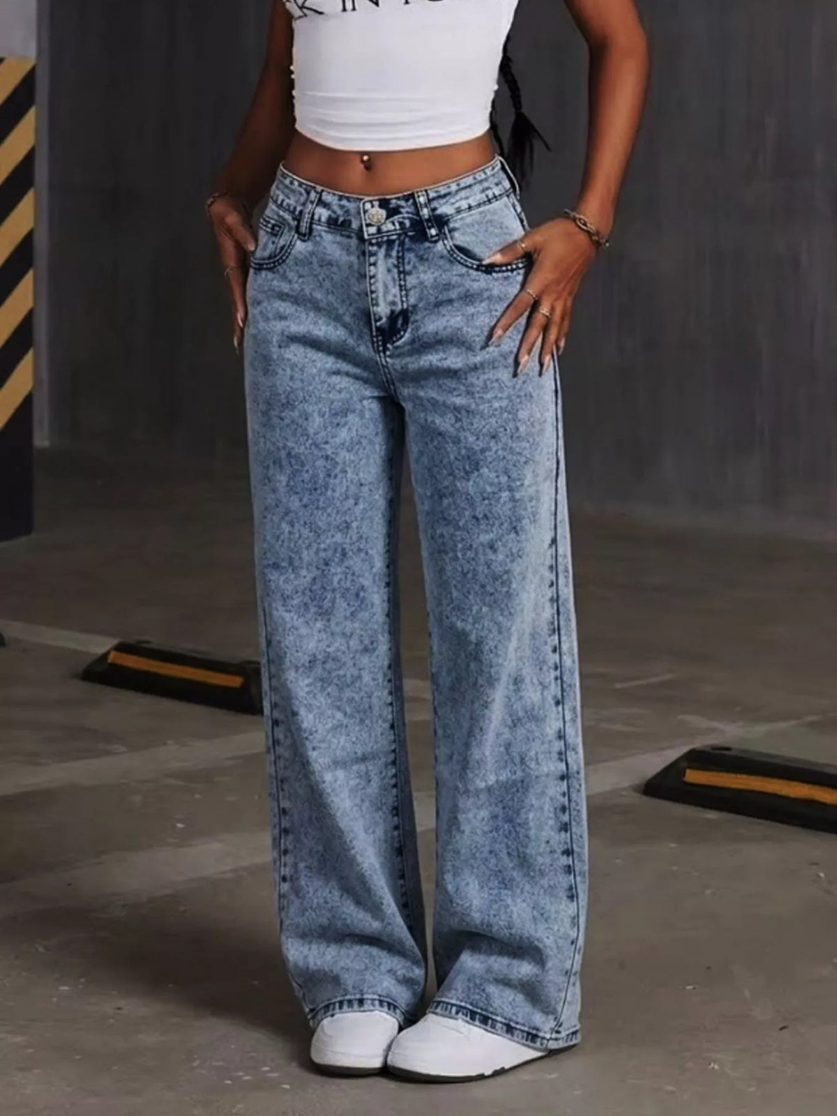 Jean bleu clair délavé à jambes larges, vu de face, porté par une mannequin tenant la taille du jean.